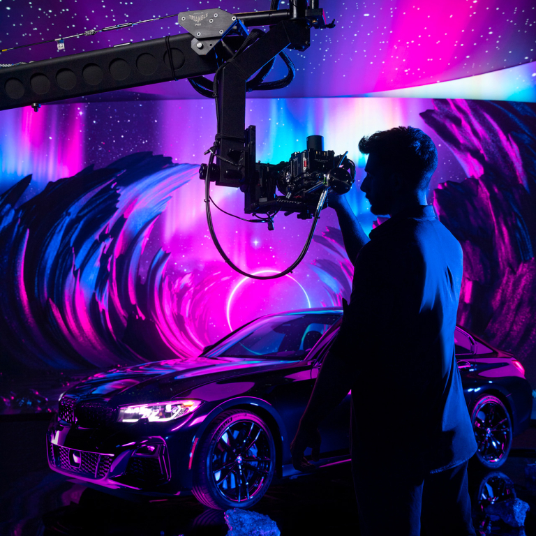 Student films car on LED volume stage against purple and magenta background.