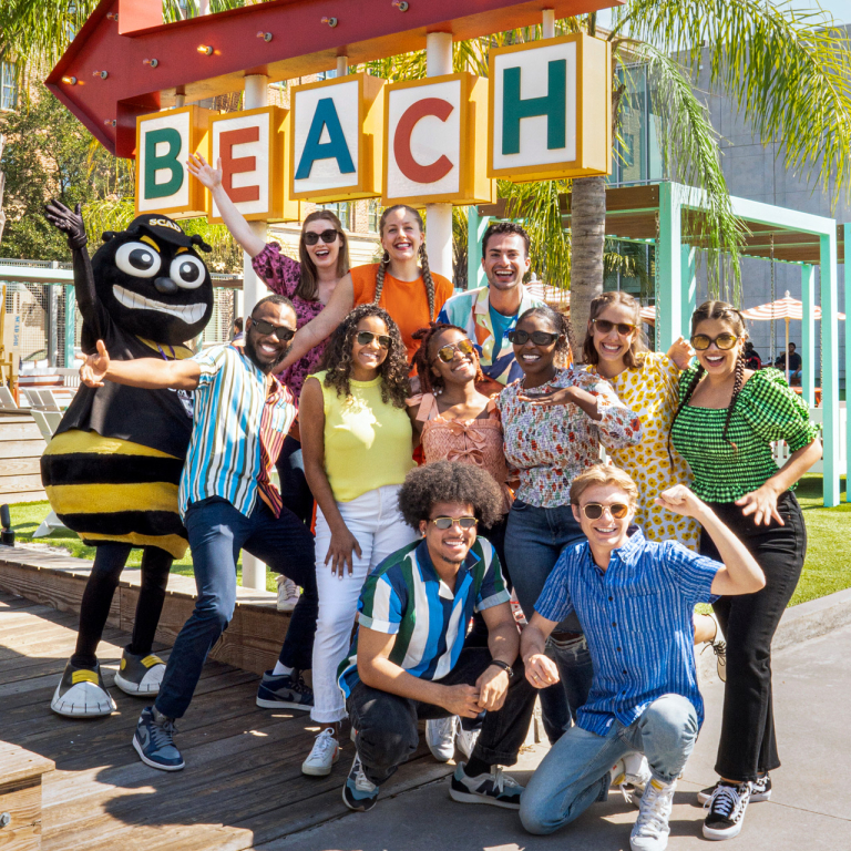 Bee Sharps at SCADDay in Savannah in fall 2022. Group smiling around the SCAD beach sign.